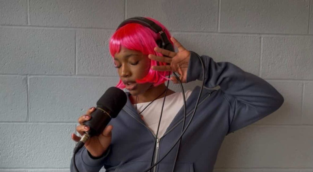 Dumebi, Nigerian singer, with pink hair holding a mic